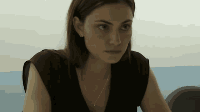 a woman wearing a necklace and earrings looks at the camera with a serious look on her face