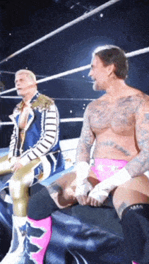 a man with a tattoo on his chest is sitting next to another man in a ring