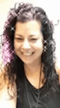 a woman with purple hair and a black shirt is smiling .
