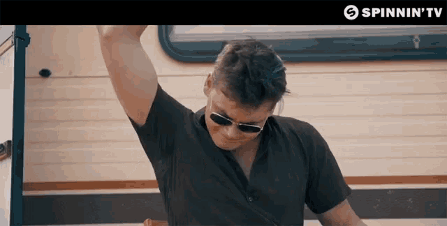 a man wearing sunglasses is dancing in front of a trailer with spinnin ' tv written above him