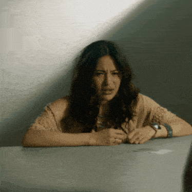 a woman sits at a table with her hands folded and a watch on her wrist