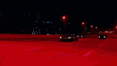 a red car is driving down the highway at night