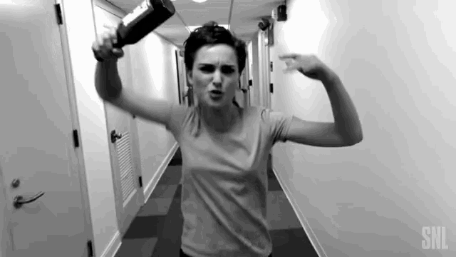 a woman flexes her muscles in a hallway with snl written on the wall