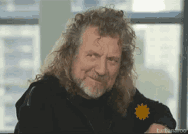 a man with long curly hair and a beard is smiling and looking at the camera .