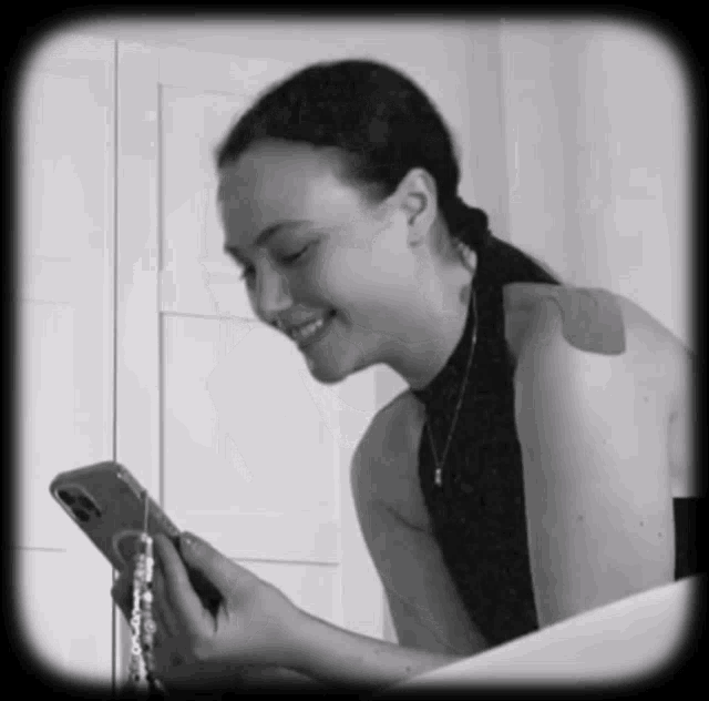 a black and white photo of a woman smiling while looking at her phone