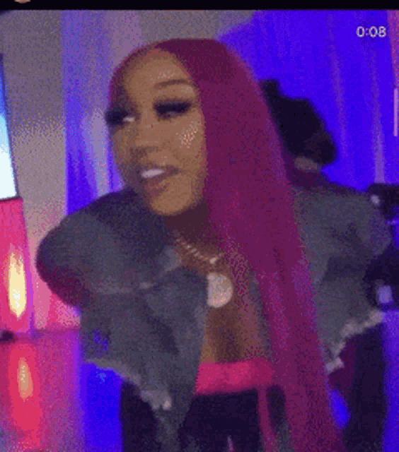 a woman with long pink hair and a denim jacket is dancing in a room .