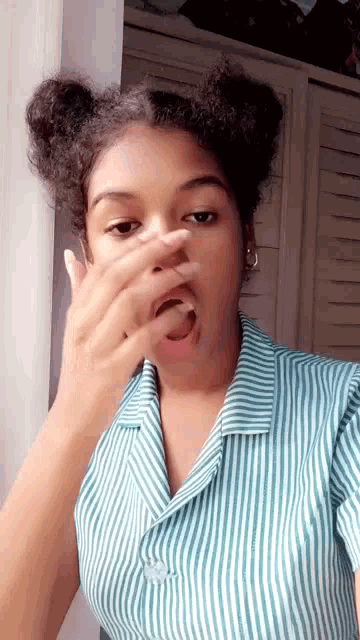 a young woman in a striped shirt is covering her face with her hand .