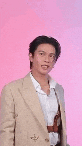 a man in a tan jacket and white shirt is standing in front of a pink background .