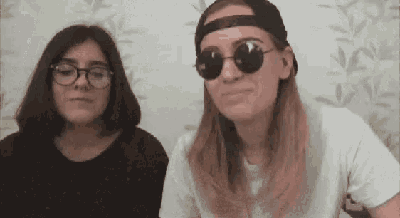 two women wearing sunglasses and a hat are sitting next to each other .