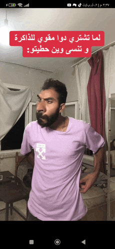 a man with a beard wearing a purple shirt is standing in a living room