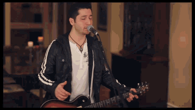 a man singing into a microphone with a guitar in front of him