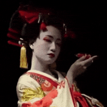 a geisha is wearing a white and red kimono and holding a red flower in her hand .