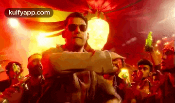 a man wearing sunglasses is standing in front of a crowd of people in a club .