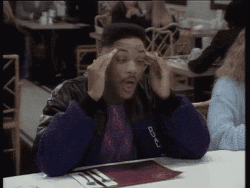 a man is sitting at a table in a restaurant with his hands on his forehead .