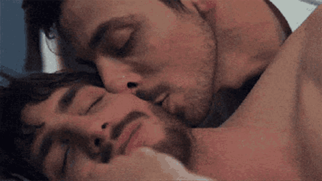 two men are kissing each other in bed while one of them is sleeping .