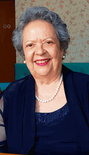 an elderly woman wearing a pearl necklace and a blue dress smiles for the camera