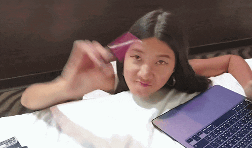 a girl is laying on a bed with a laptop and a credit card