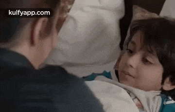 a young boy is laying in a bed with a man standing next to him .
