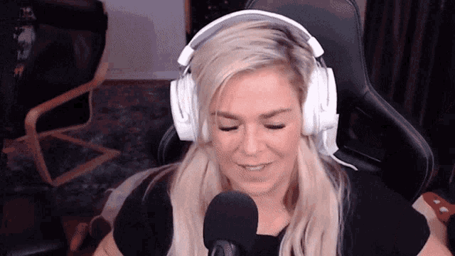 a woman wearing headphones and a black shirt is smiling in front of a microphone .
