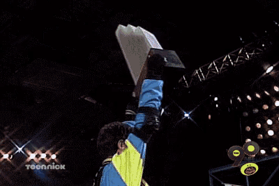 a man in a blue and yellow jacket is holding a laptop up in the air in front of a sign that says techniok