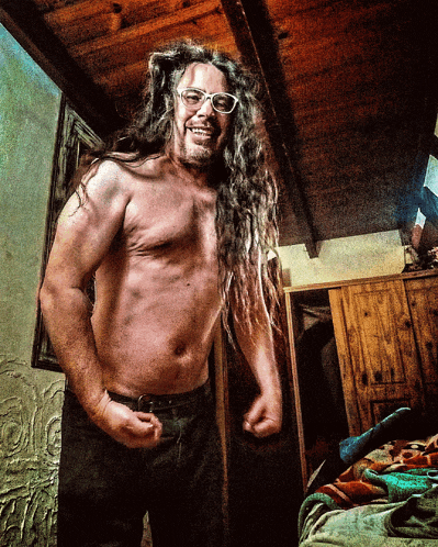a shirtless man with long dreadlocks and glasses stands in a room