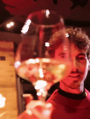 a man in a red shirt is holding up a glass of wine