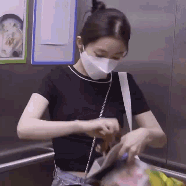 a woman wearing a mask is standing in an elevator and holding a bag .
