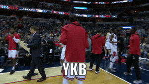 a man in a red jacket is walking on a basketball court with ykb written on the bottom