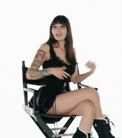 a woman is sitting in a director 's chair with her legs crossed and a tattoo on her arm .