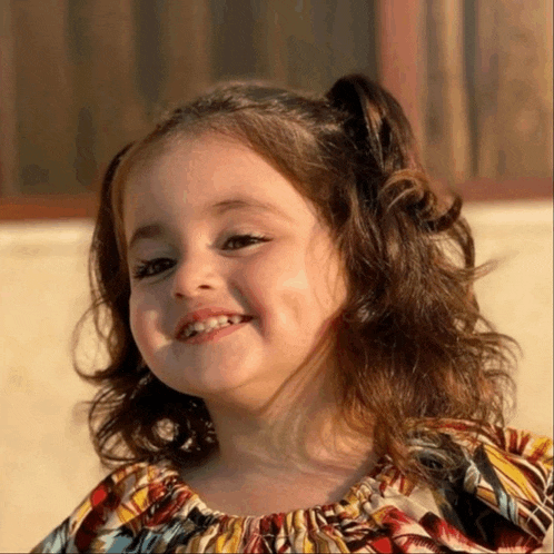 a little girl with pigtails is smiling and wearing a striped shirt