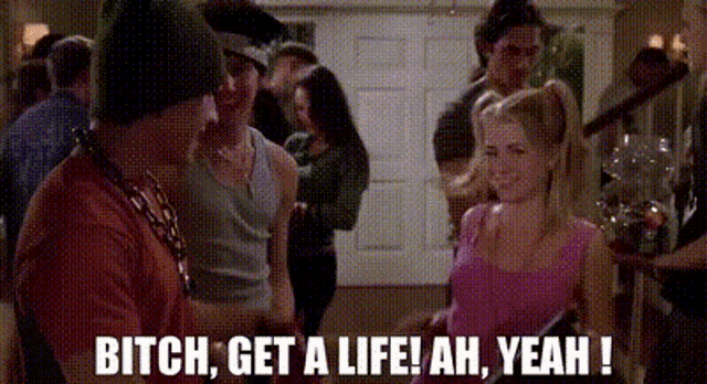 a group of people are standing in a room and a woman is talking to a man in a hat .