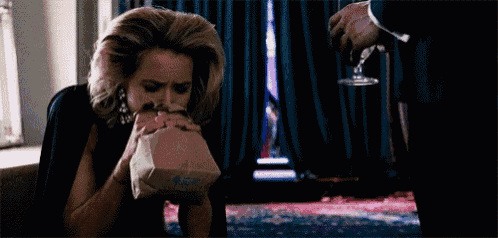 a woman is sitting on the floor with a bag in her mouth and a man is holding a glass of wine .