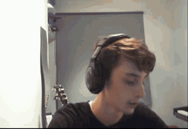 a young man wearing headphones is playing a guitar in a room .