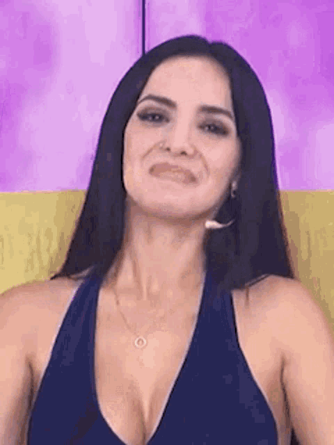 a woman in a blue tank top is sitting on a yellow chair making a funny face .