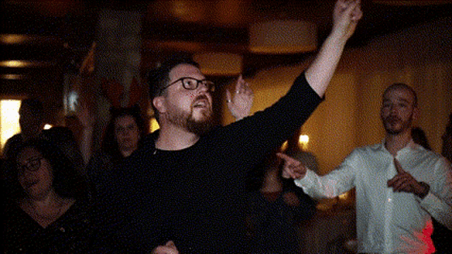 a man with glasses is dancing in front of a crowd of people