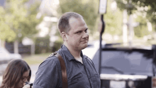 a man in a gray shirt with a brown strap on his shoulder is walking down the street .