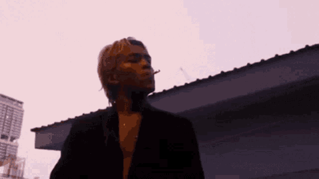 a man in a black jacket is smoking a cigarette while standing in front of a building .