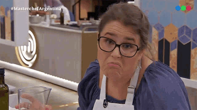 a woman wearing glasses and an apron is making a funny face in front of a masterchef argentina logo