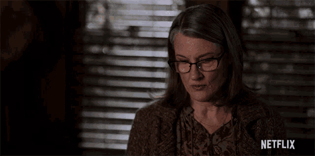 a woman wearing glasses is sitting in front of a window with a netflix logo on the bottom right