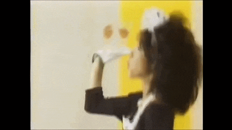 a woman in a maid costume is blowing a kiss while standing in front of a yellow wall .