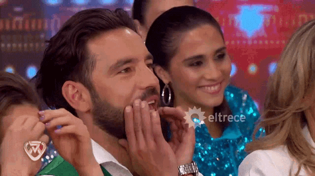 a man with a beard is laughing in a crowd with eltrece written on the bottom right