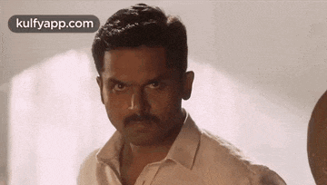 a man with a mustache and a white shirt is making a funny face .