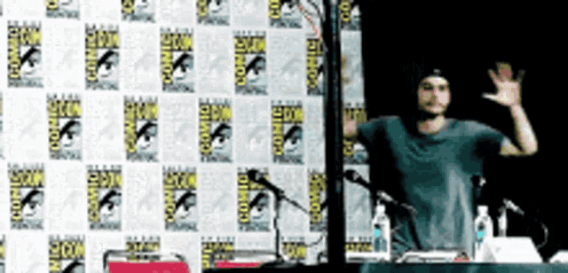 a man is standing in front of a comic con wall