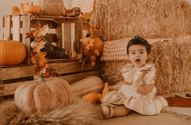 a little girl in a dress is sitting in front of a pile of hay and pumpkins