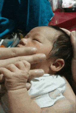 a baby is being held in a person 's arms and their hand is on the baby 's face