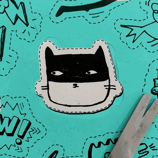 a pair of scissors is cutting a sticker of a cat wearing a batman mask
