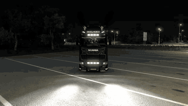 a black scania truck is parked in a parking lot at night