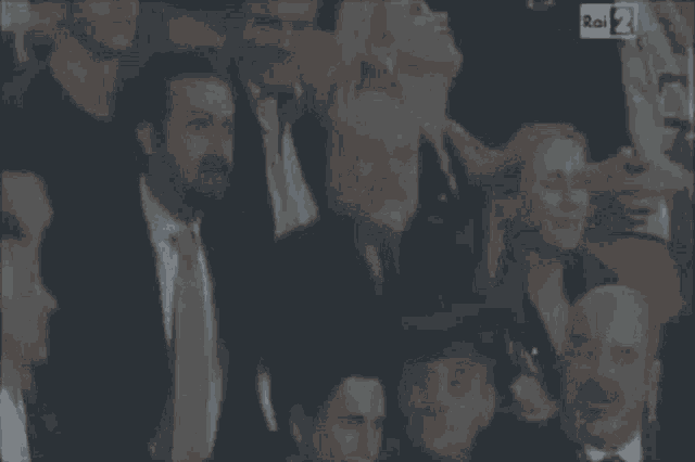 a group of people are gathered in a dark room with rai 2 on the bottom left