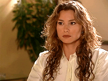 a woman with long curly hair is wearing a white shirt and earrings