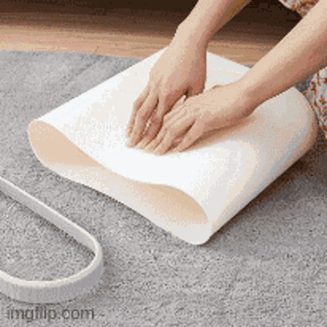 a person 's hands are on a piece of white paper on a rug